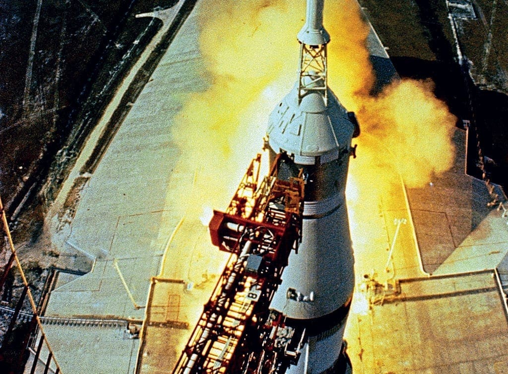 Apollo 11. Seconds before lift-off, a fish-eye lens camera high up on the Launch Umbilical Tower casts a dramatic view of the five F-1 engines running up to full thrust before release. Note the white boost protective cover (BPC) supporting the launch escape system (LES) encapsulating the Command Module. (NASA)